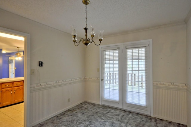 empty room featuring a wainscoted wall, crown molding, a textured ceiling, and an inviting chandelier