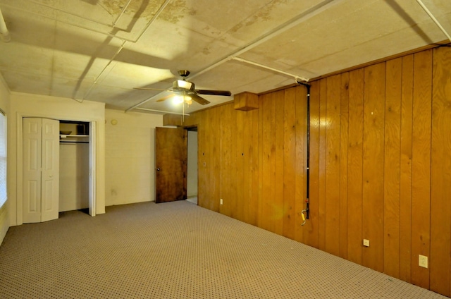 unfurnished bedroom with carpet floors, a closet, wooden walls, and a ceiling fan