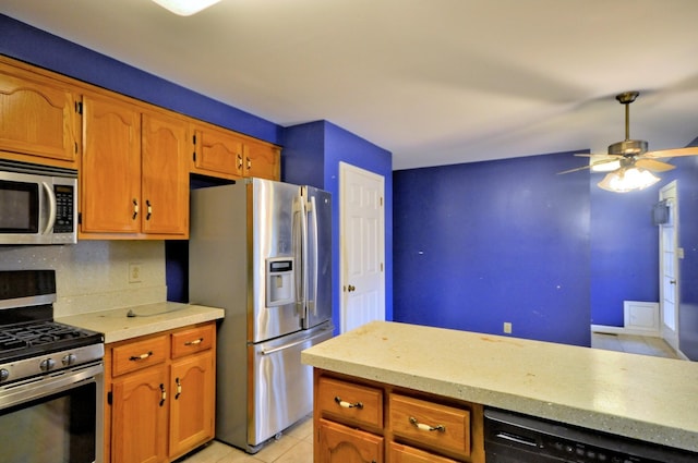 kitchen featuring light tile patterned floors, a ceiling fan, appliances with stainless steel finishes, brown cabinets, and light countertops