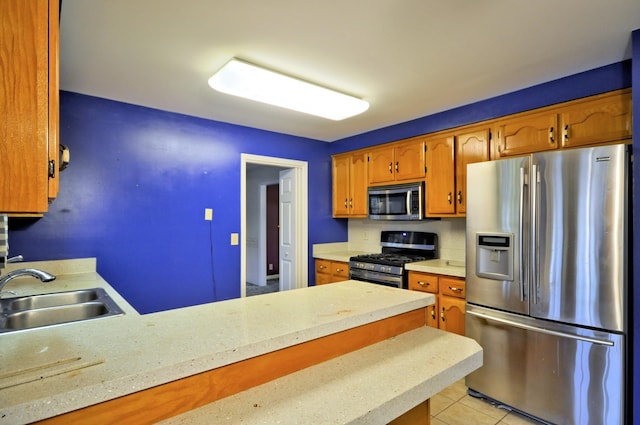 kitchen with light tile patterned flooring, a peninsula, a sink, light countertops, and appliances with stainless steel finishes