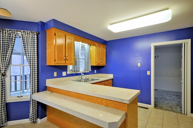 kitchen featuring a peninsula, light tile patterned floors, light countertops, and a sink