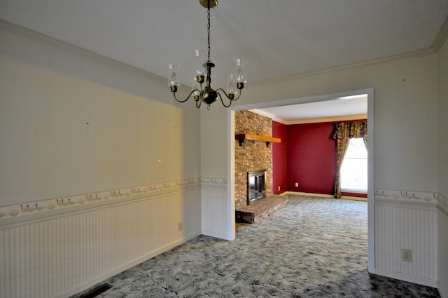 unfurnished living room with a wainscoted wall, crown molding, a fireplace, a notable chandelier, and carpet flooring