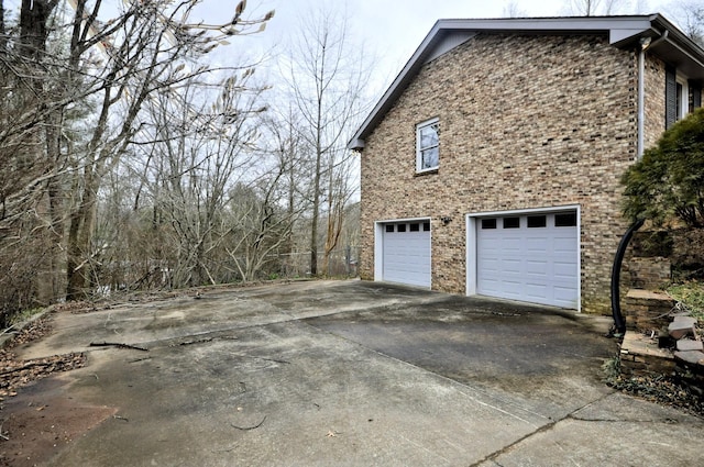 view of side of property featuring a garage, concrete driveway, and brick siding