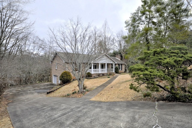 view of front of home featuring covered porch, aphalt driveway, a chimney, and a garage