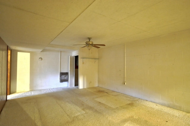 carpeted spare room with concrete block wall and a ceiling fan