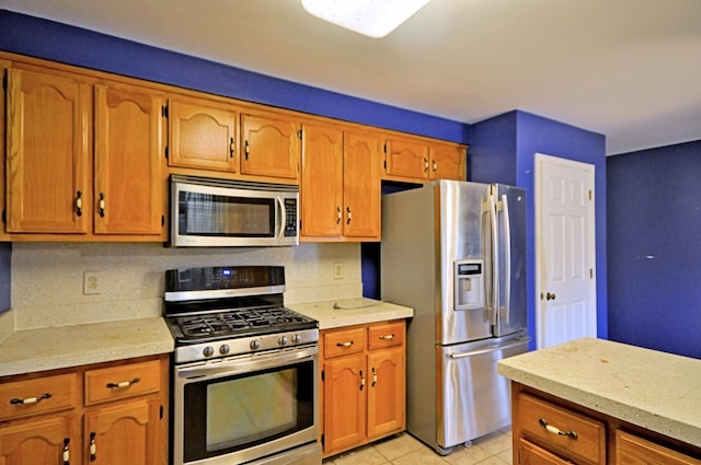 kitchen featuring brown cabinets, light tile patterned floors, stainless steel appliances, light countertops, and decorative backsplash