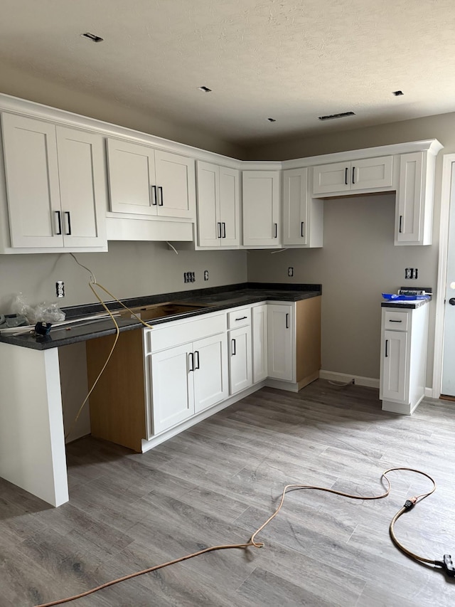 kitchen with dark countertops, visible vents, white cabinetry, light wood-type flooring, and baseboards