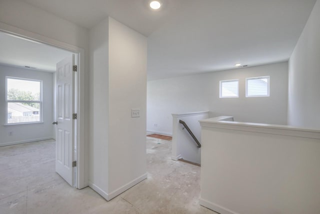 corridor featuring baseboards, a healthy amount of sunlight, and an upstairs landing