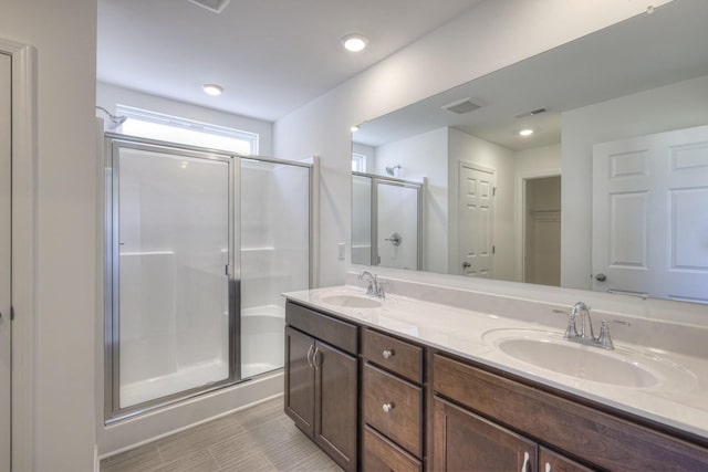 full bathroom with visible vents, a sink, a shower stall, and double vanity