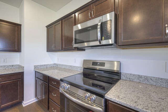 kitchen with stainless steel appliances, dark brown cabinetry, and light stone counters