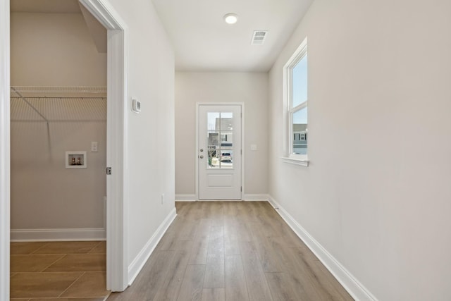 doorway with light wood-type flooring, visible vents, and baseboards