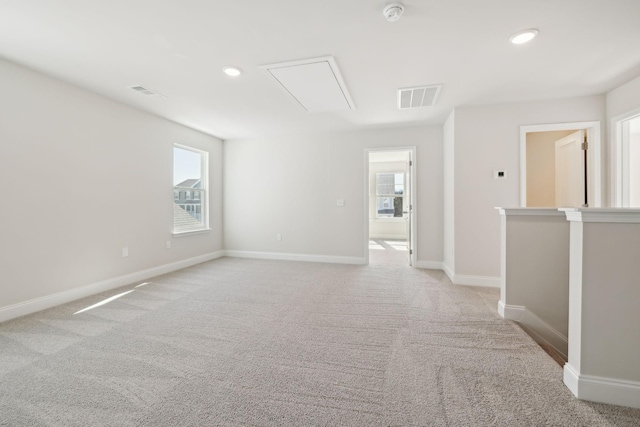 empty room with attic access, visible vents, light carpet, and baseboards