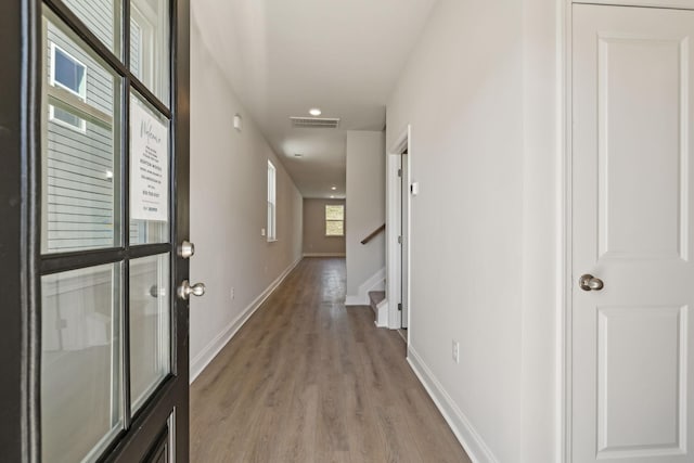 hallway with light wood-type flooring, visible vents, stairway, and baseboards