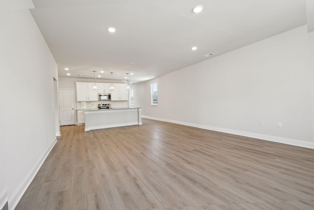 unfurnished living room featuring light wood finished floors, recessed lighting, and baseboards