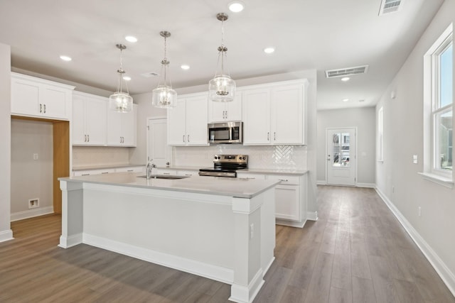 kitchen with stainless steel appliances, a sink, visible vents, light countertops, and an island with sink