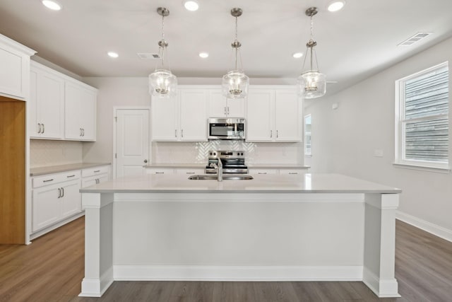 kitchen with a center island with sink, appliances with stainless steel finishes, light countertops, white cabinetry, and a sink