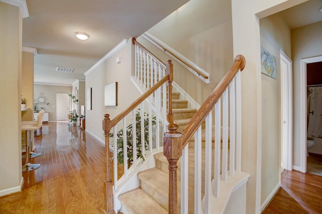 staircase with hardwood / wood-style flooring, baseboards, visible vents, and ornamental molding