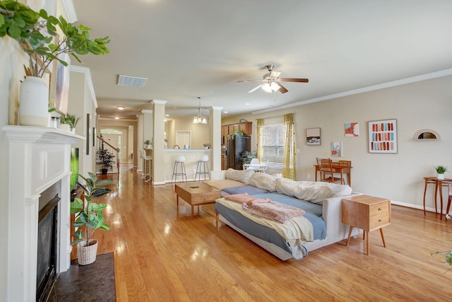 living room with a fireplace with flush hearth, visible vents, wood finished floors, and ornamental molding