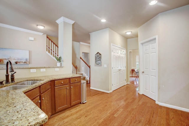 kitchen with light stone counters, light wood finished floors, brown cabinetry, ornamental molding, and a sink