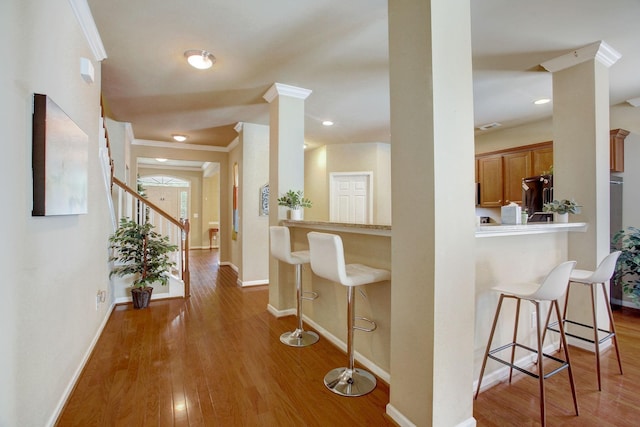 hall with baseboards, ornamental molding, wood finished floors, stairs, and ornate columns