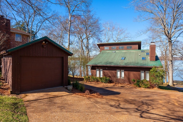 chalet / cabin featuring driveway, a garage, a chimney, metal roof, and an outdoor structure