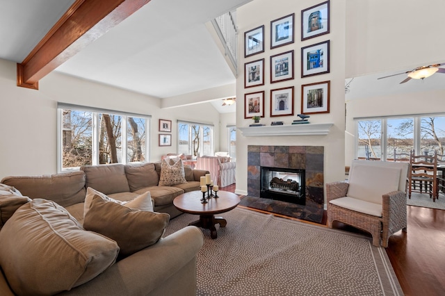 living room featuring beam ceiling, a ceiling fan, wood finished floors, and a tiled fireplace