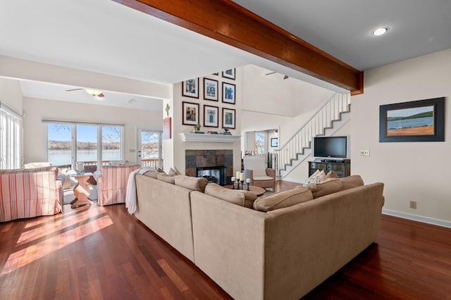 living room featuring baseboards, a tiled fireplace, stairway, dark wood-type flooring, and beamed ceiling