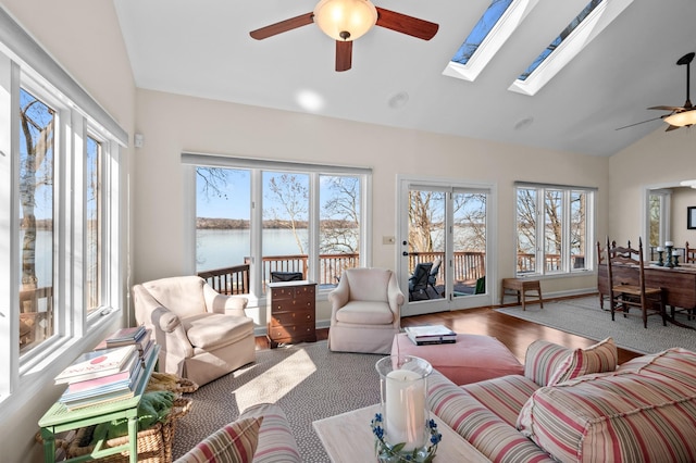 living room with ceiling fan, lofted ceiling with skylight, a water view, and baseboards