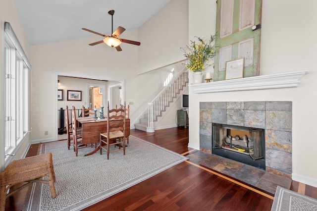 dining room with a fireplace, stairway, wood finished floors, high vaulted ceiling, and baseboards