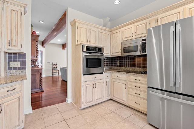 kitchen featuring light stone counters, light tile patterned floors, cream cabinets, decorative backsplash, and appliances with stainless steel finishes