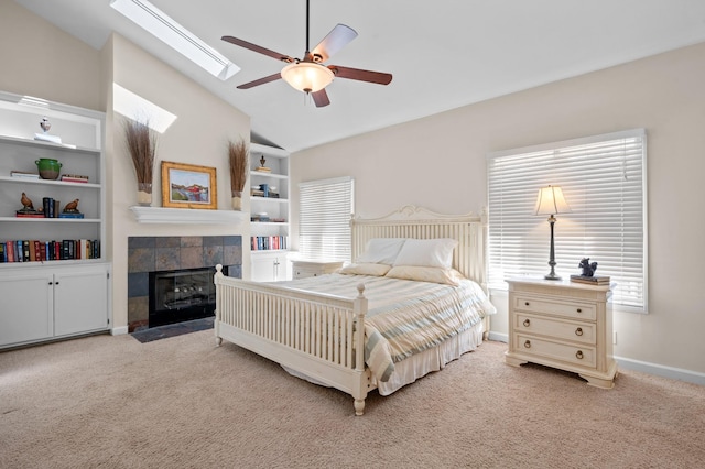 carpeted bedroom featuring lofted ceiling with skylight, a tile fireplace, ceiling fan, and baseboards