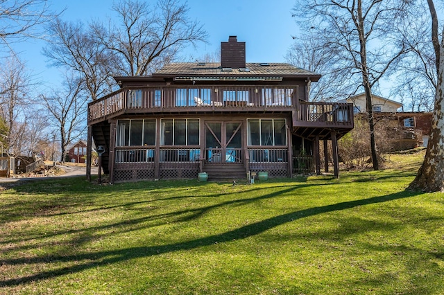 rear view of house featuring a chimney, a sunroom, a lawn, and a deck