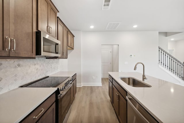 kitchen with appliances with stainless steel finishes, light countertops, a sink, and backsplash