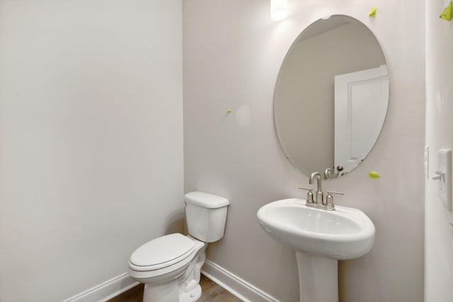 half bath with a sink, toilet, baseboards, and wood finished floors