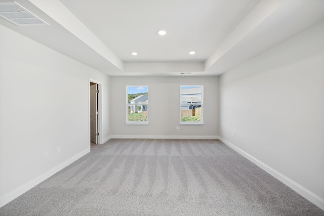 empty room with baseboards, visible vents, a raised ceiling, and light colored carpet