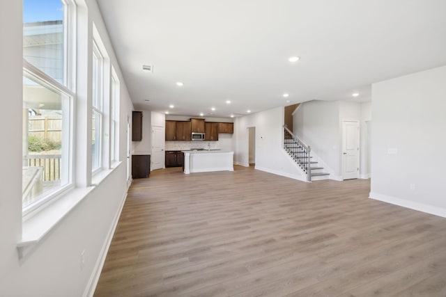 unfurnished living room featuring light wood-style floors, recessed lighting, baseboards, and stairs