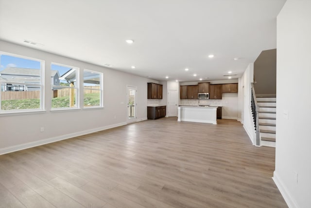 unfurnished living room with stairway, plenty of natural light, light wood-style flooring, and recessed lighting