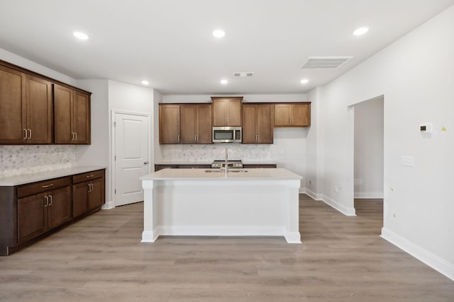 kitchen with light wood finished floors, visible vents, a kitchen island with sink, and stainless steel microwave