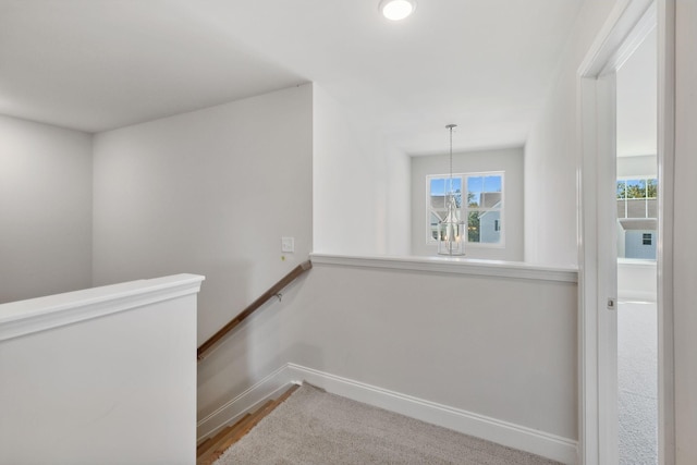 corridor with baseboards, a notable chandelier, and an upstairs landing