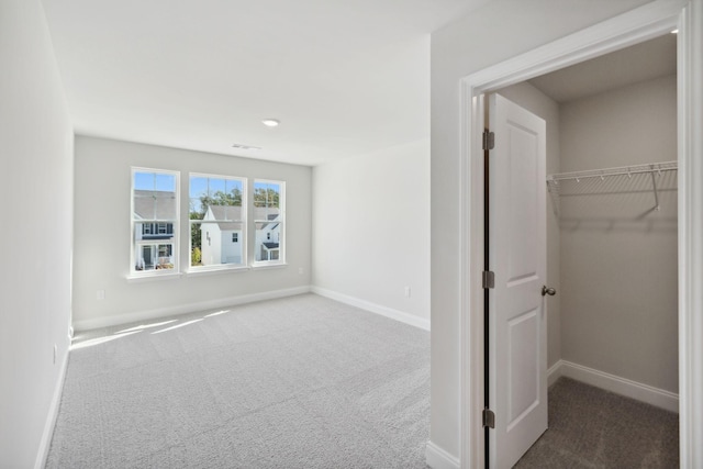 unfurnished bedroom with carpet floors, a closet, a walk in closet, and baseboards