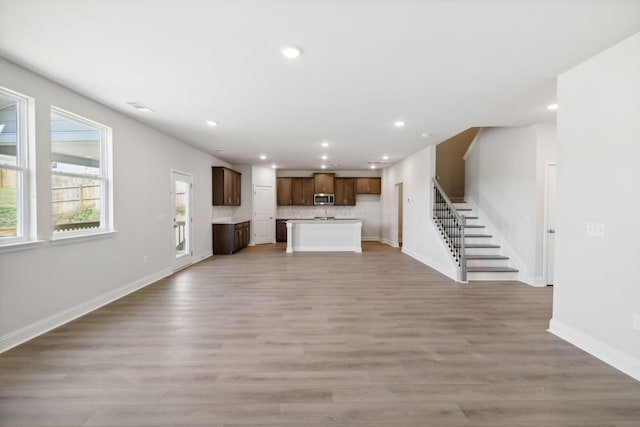 unfurnished living room featuring baseboards, visible vents, stairway, light wood-type flooring, and recessed lighting