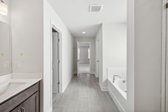 bathroom featuring tile patterned flooring, vanity, visible vents, baseboards, and a bath