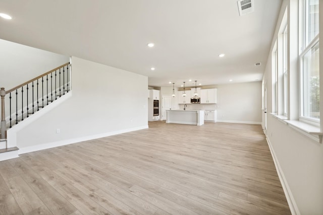 unfurnished living room with light wood-style flooring, stairway, visible vents, and baseboards