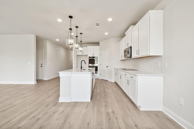 kitchen with appliances with stainless steel finishes, a sink, light wood-style flooring, and decorative backsplash