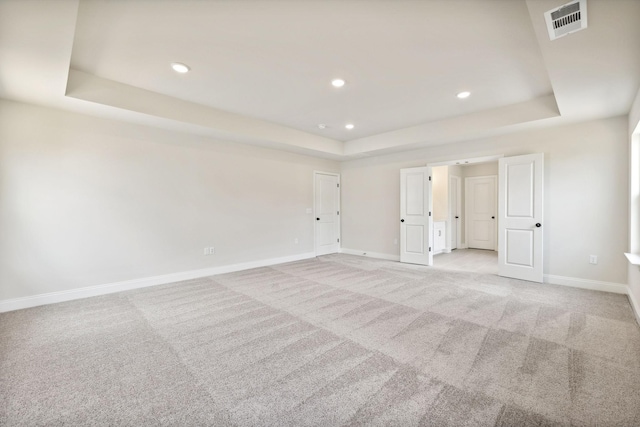 unfurnished bedroom featuring a tray ceiling, light colored carpet, visible vents, and baseboards