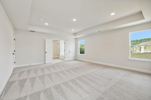 empty room featuring a raised ceiling, light carpet, and baseboards