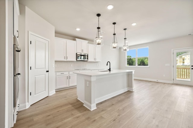 kitchen featuring light wood-type flooring, tasteful backsplash, stainless steel microwave, and light countertops