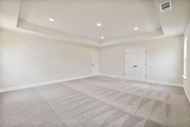 spare room featuring light carpet, a raised ceiling, visible vents, and baseboards