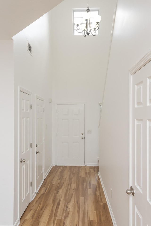 hall featuring a chandelier, visible vents, a towering ceiling, baseboards, and light wood finished floors