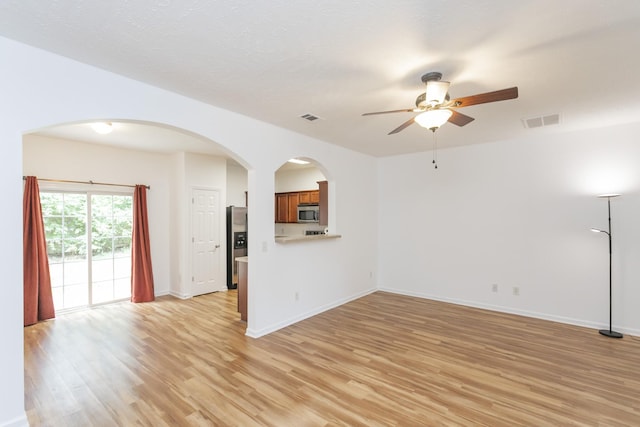 unfurnished living room featuring arched walkways, visible vents, light wood-style flooring, and baseboards